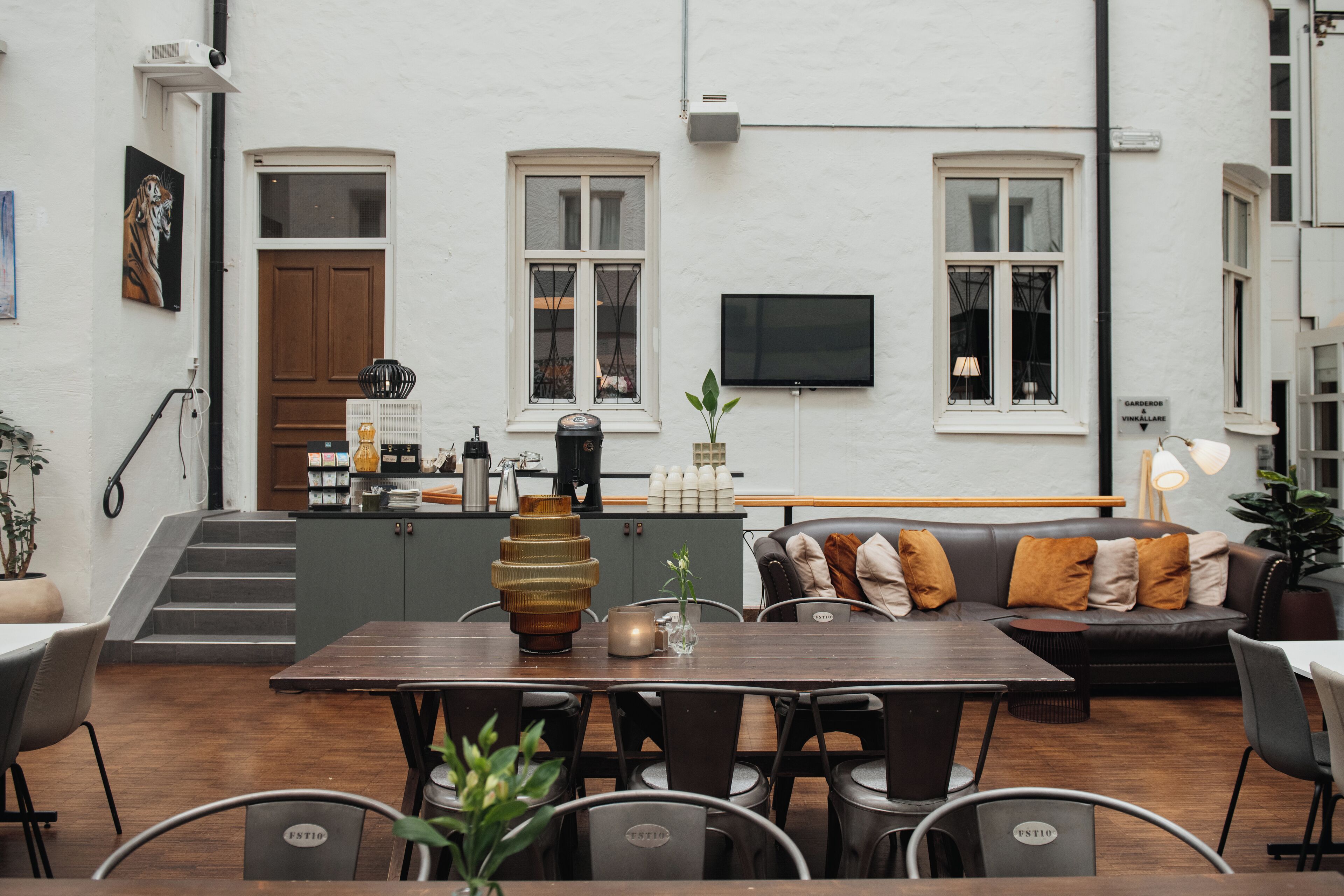 A modern outdoor seating area with a wooden table and chairs, a sofa with cushions, and a flat-screen TV mounted on the wall.