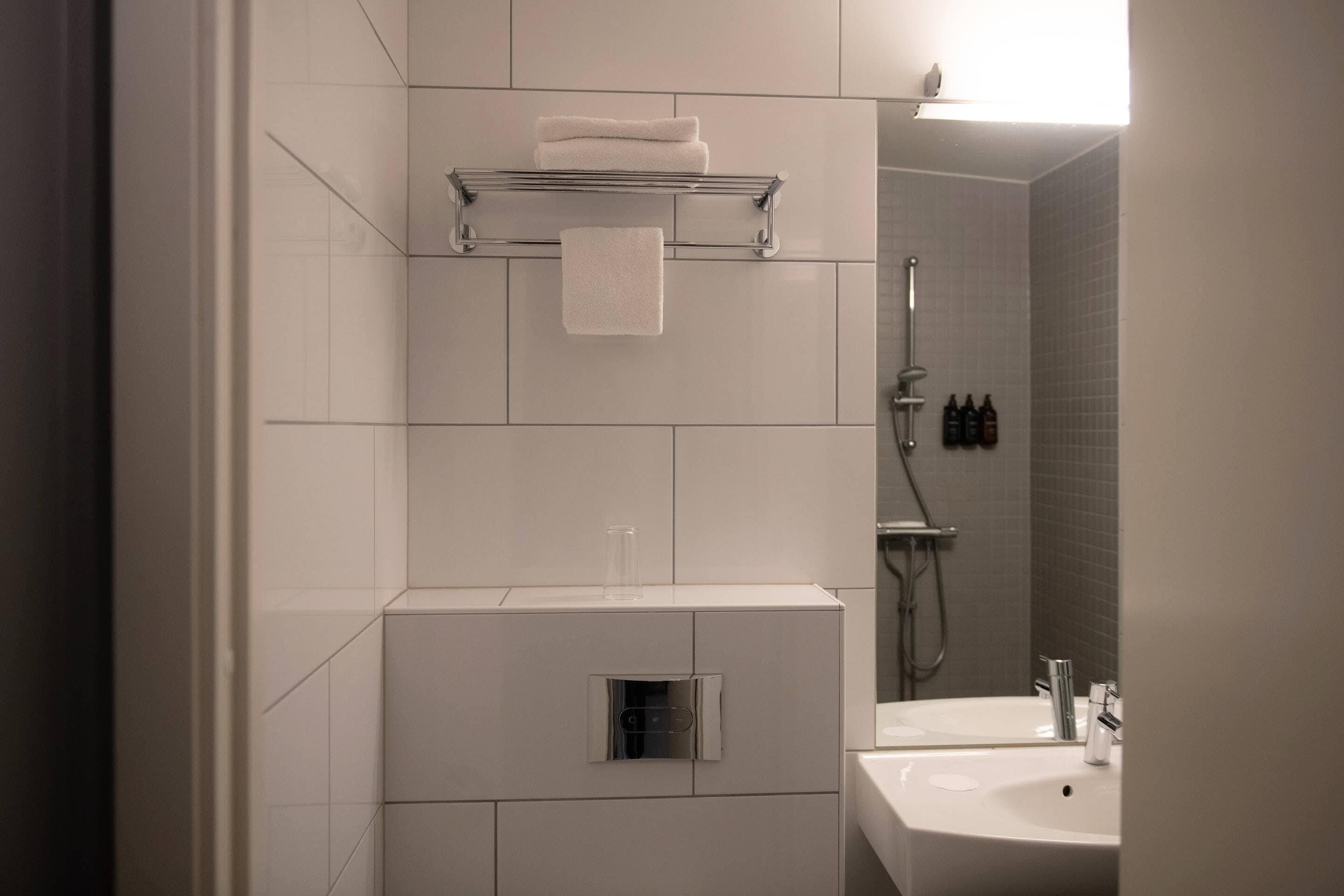 A modern bathroom with a white tiled wall, a glass shower enclosure, a built-in sink, and a towel rack.