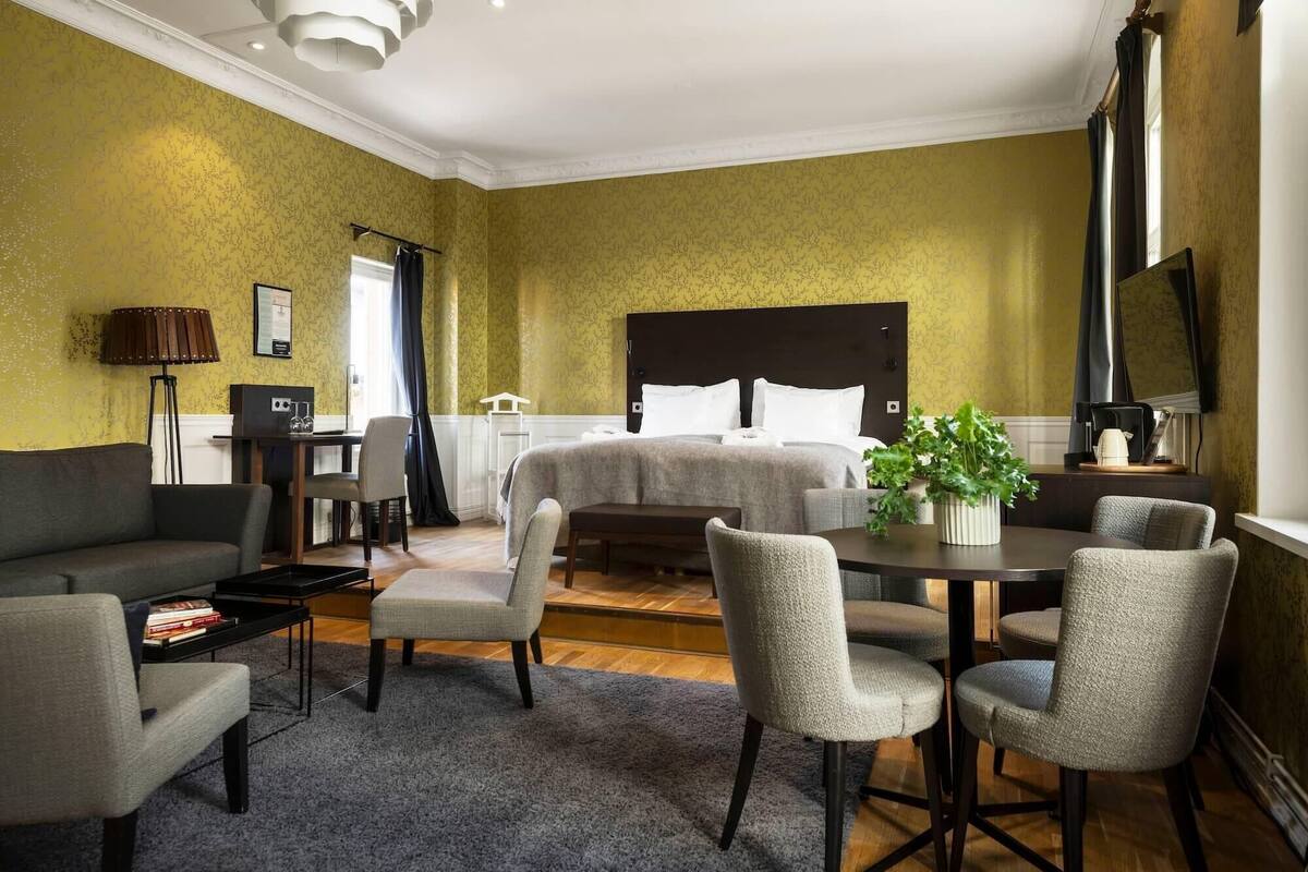 A hotel room with a large bed, a desk with a chair, a sofa, and a small table with chairs.