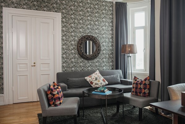 A living room with a grey sofa, two armchairs, a coffee table, and a mirror on the wall. - Home Hotel Plaza (Karlstad)