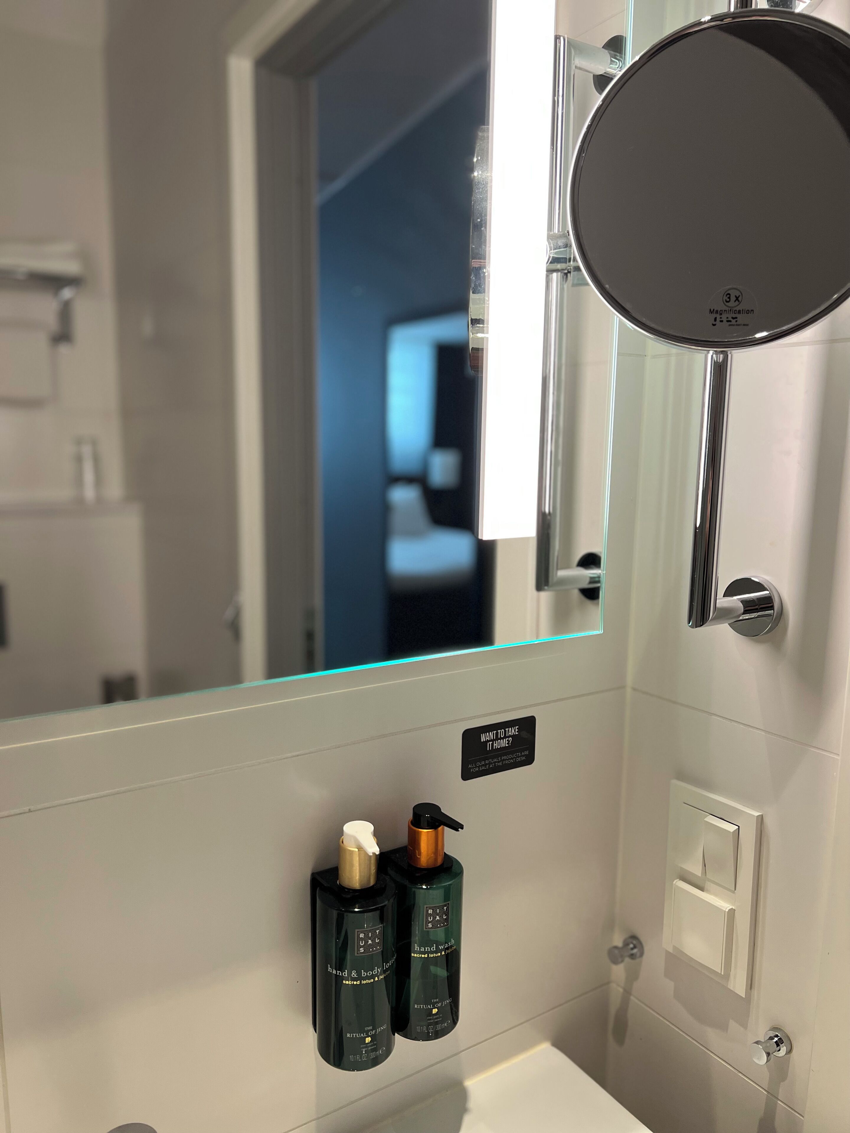 A bathroom with a large mirror, a hand soap dispenser, and a hand lotion bottle.
