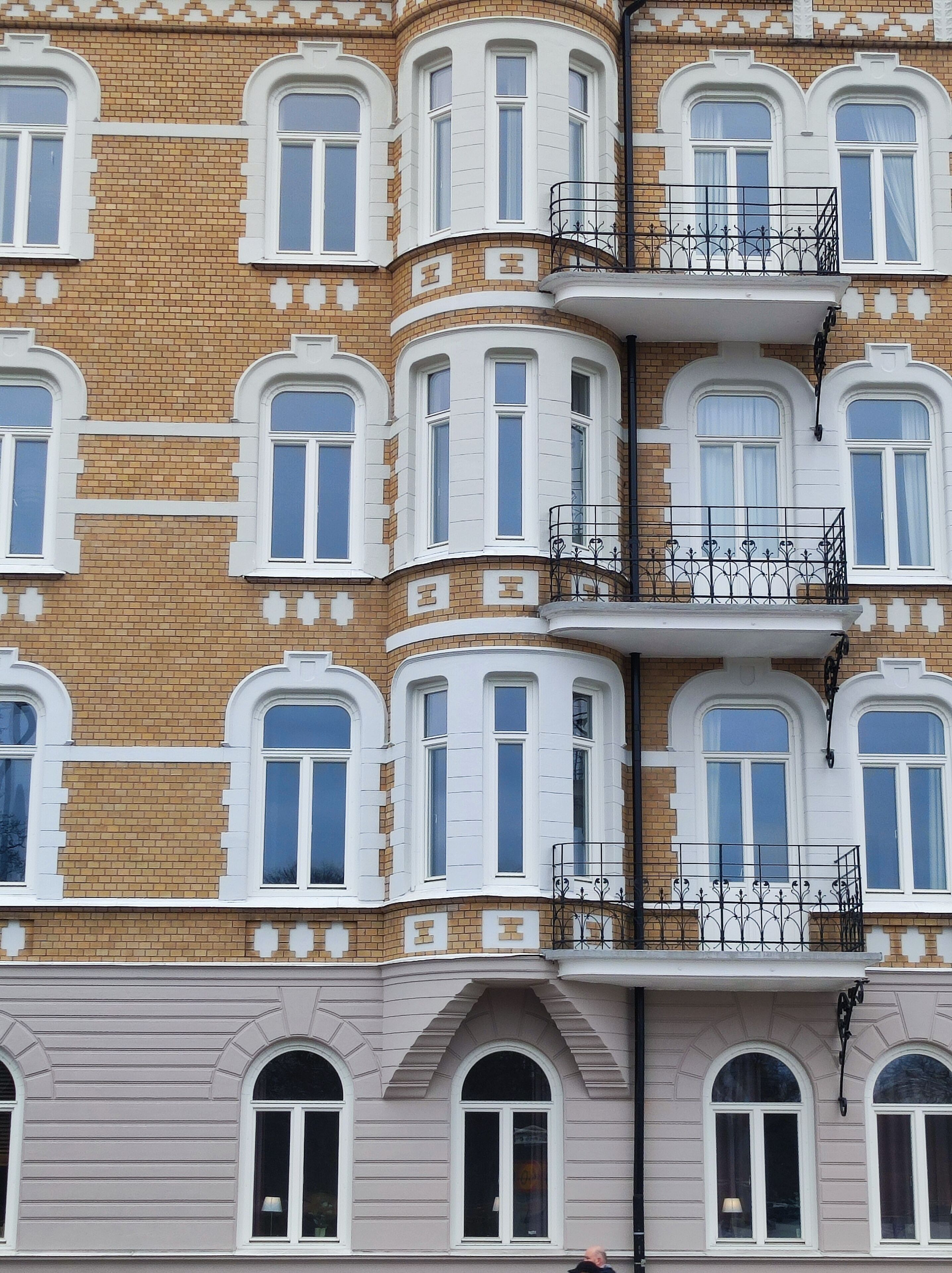 Un edificio de varios pisos con fachada de ladrillo, ventanas con marcos blancos y un balcón con barandilla metálica.