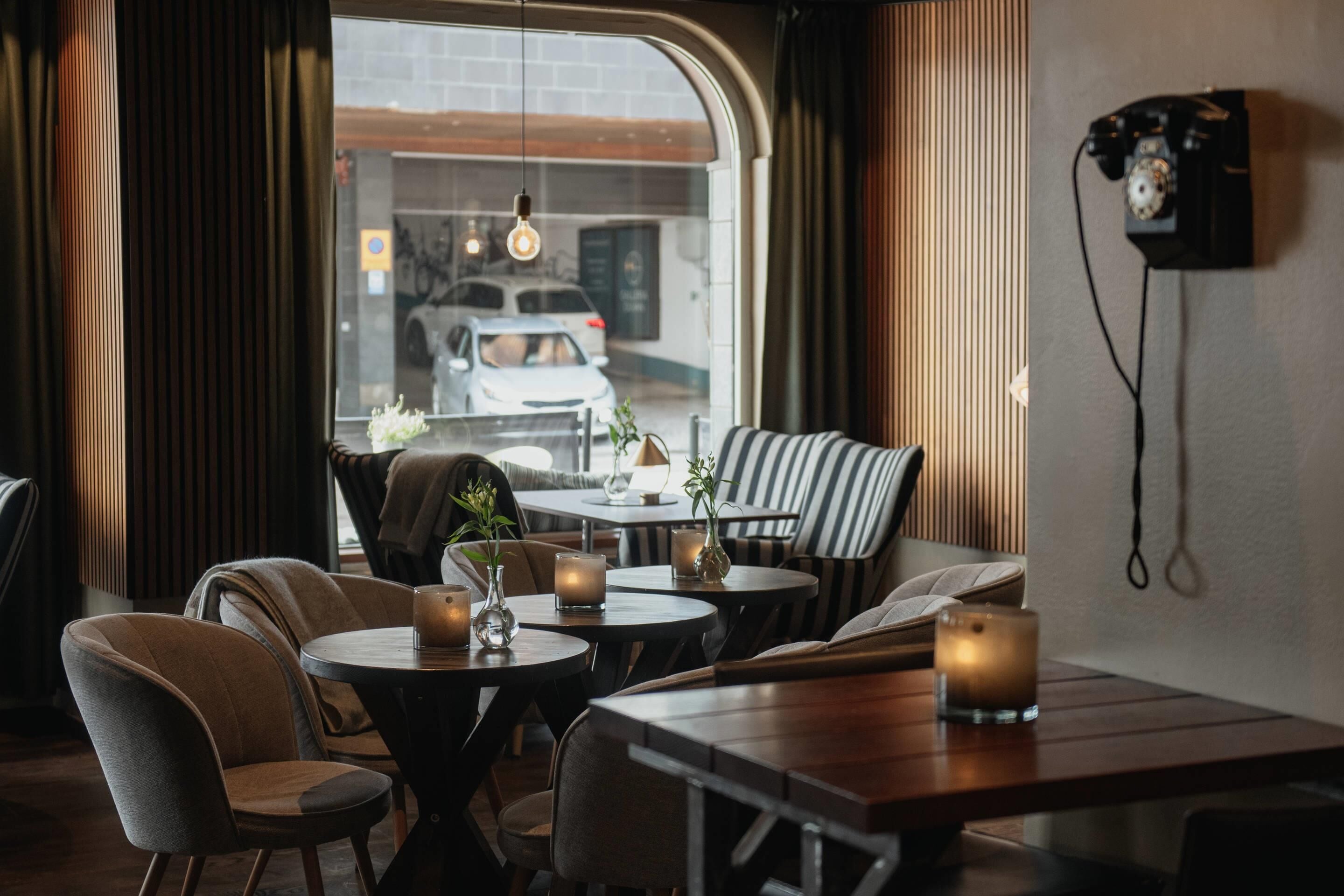 A cozy dining area with round tables, chairs, and candles. A vintage telephone hangs on the wall.