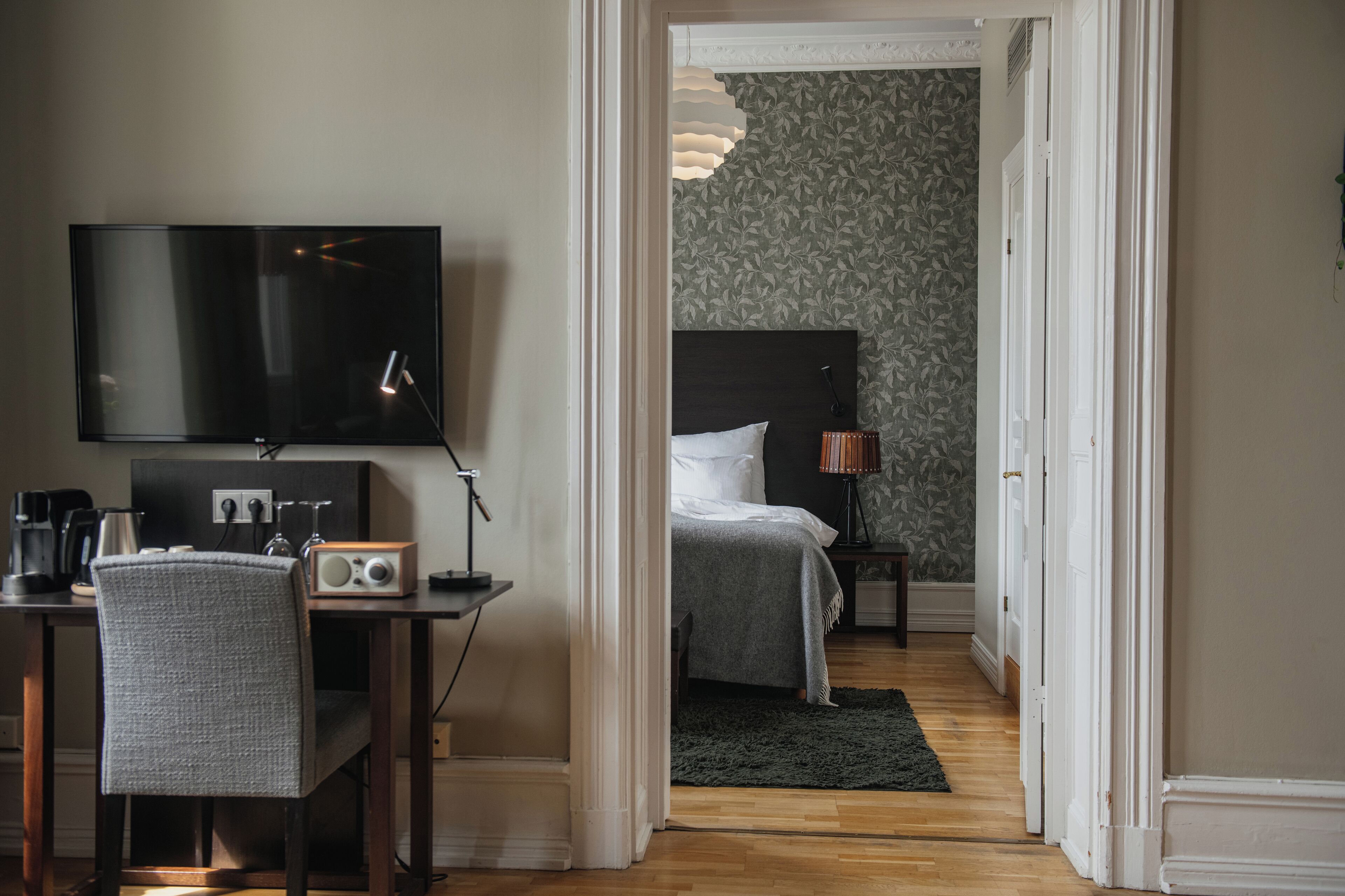 A hotel room with a bed, a desk with a chair, a television, and a lamp.