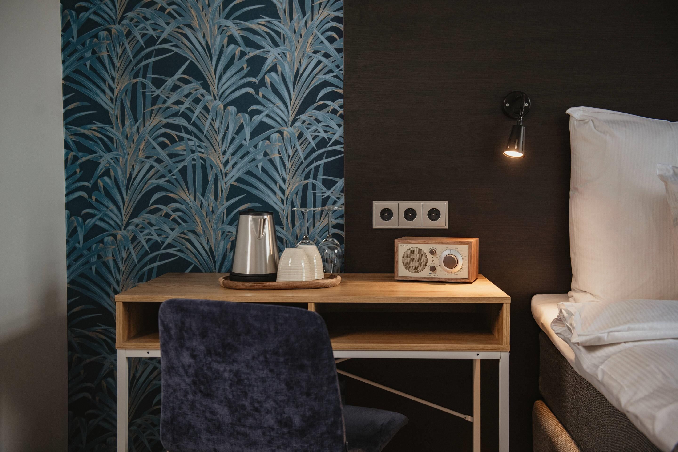 A compact room with a bed, a small desk with a radio, and a wall with a blue leafy pattern.