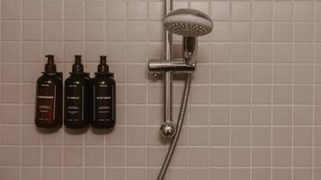 A shower with a handheld showerhead and a wall-mounted control valve. Three bottles of toiletries are visible on the wall.
