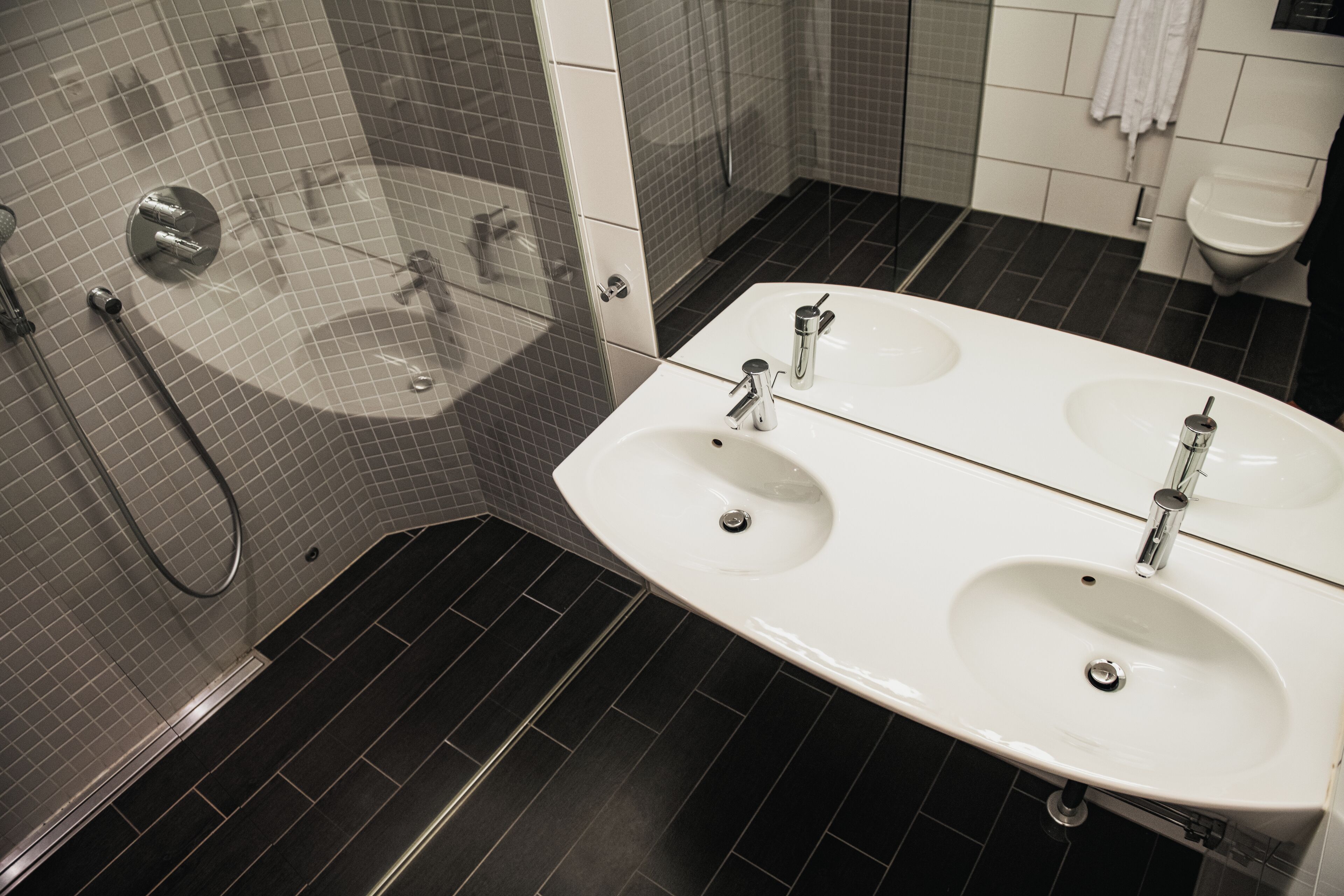 A modern bathroom with a large white sink, a glass-enclosed shower, and dark tiled flooring.