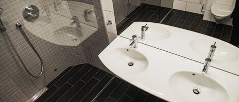 A modern bathroom with a large white sink, a glass-enclosed shower, and dark tiled flooring.