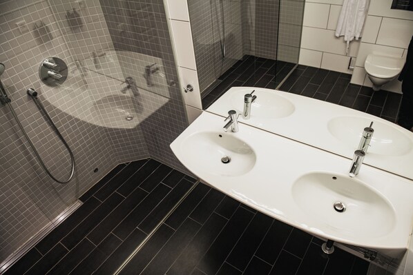 A modern bathroom with a large white sink, a glass-enclosed shower, and dark tiled flooring.