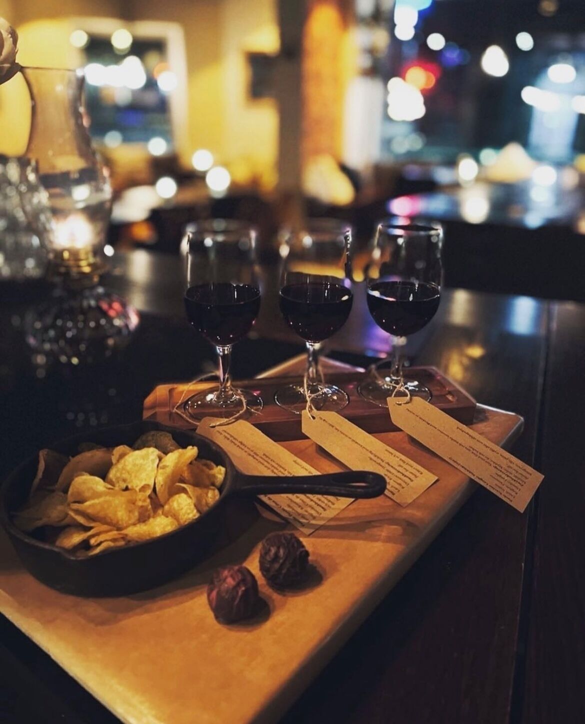 A bar setting with three glasses of red wine, a bowl of chips, and a bottle of liquor.
