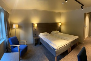 A hotel room with a double bed, a chair, a small table, and a lamp.
