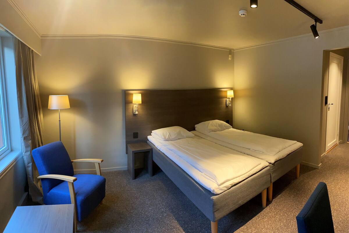 Una habitación de hotel con una cama individual, una silla, una mesita y una lámpara.