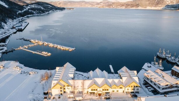 Un bâtiment enneigé avec une jetée qui s’avance sur un lac paisible, le tout entouré de montagnes.