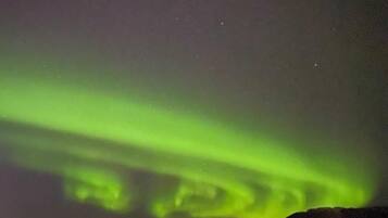 Vista nocturna de las auroras boreales sobre una masa de agua tranquila, con barcos y luces distantes.