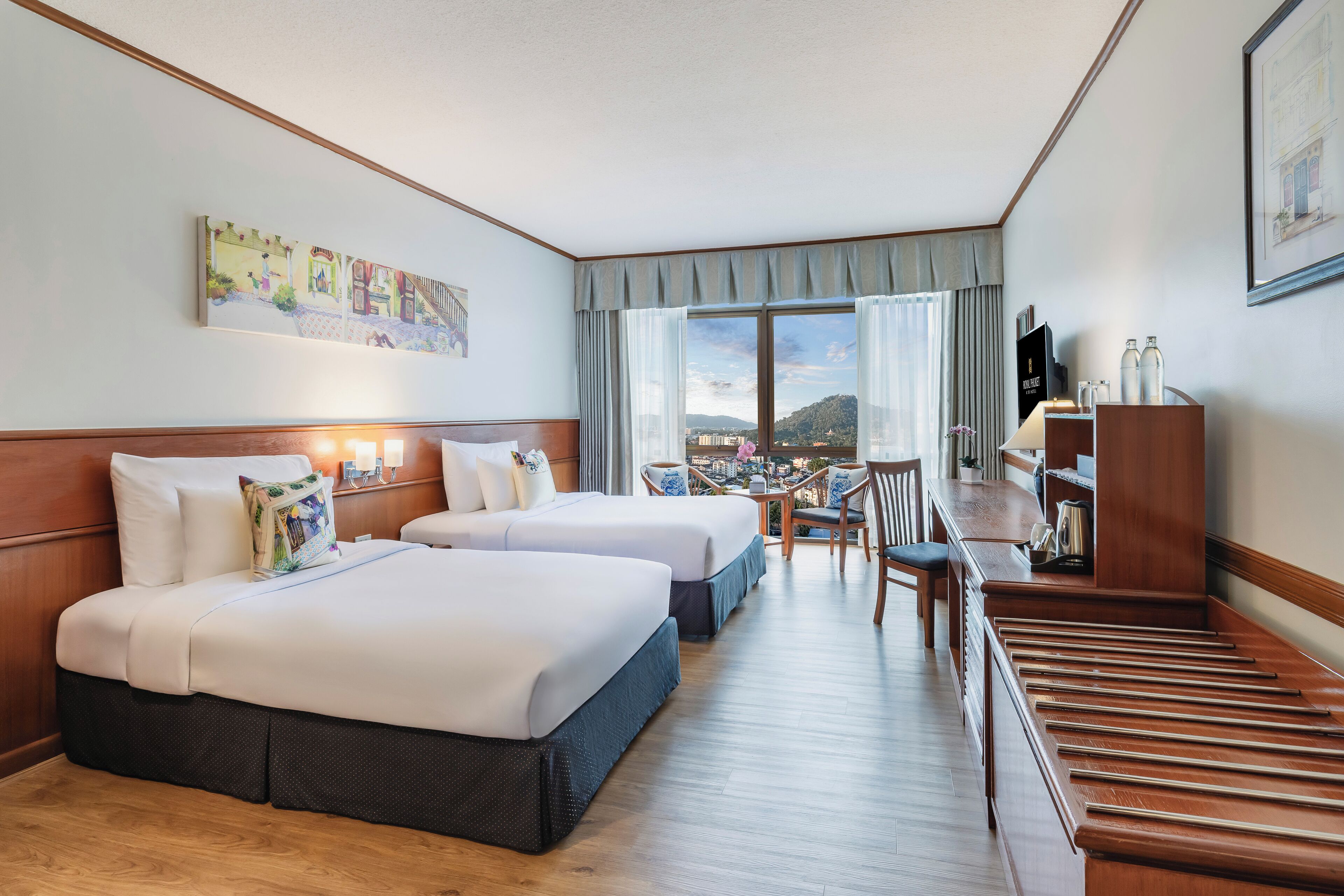 A hotel room with two beds, a dining table, and a view of a cityscape.