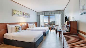 A hotel room with two beds, a dining table, and a view of a cityscape.