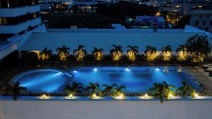 Piscina con jardín circundante y palmeras, con edificios de fondo.