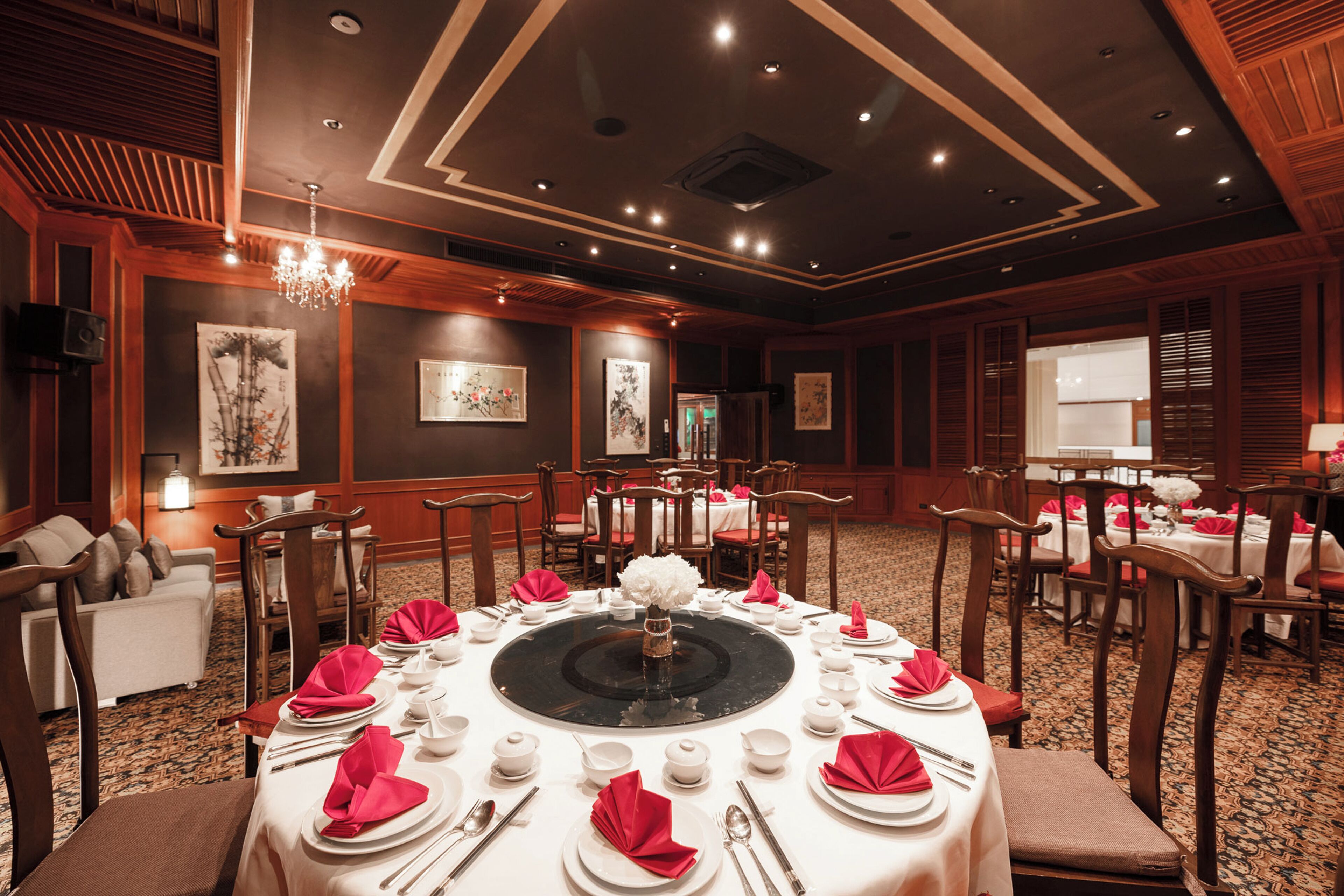 A formal dining room with round tables, red napkins, and white table settings.