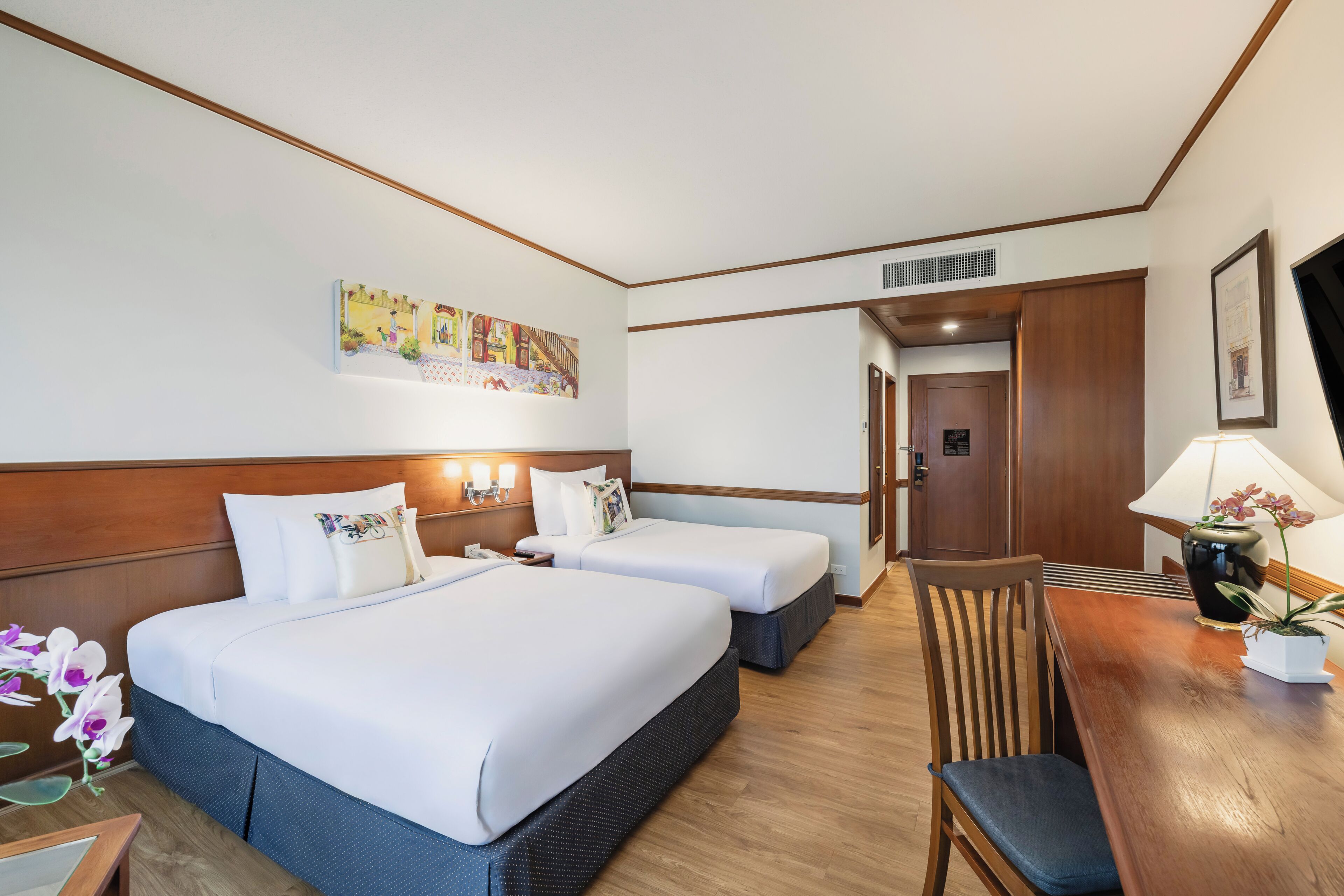 A hotel room with two beds, a wooden dining table, a chair, a TV, and a painting on the wall.