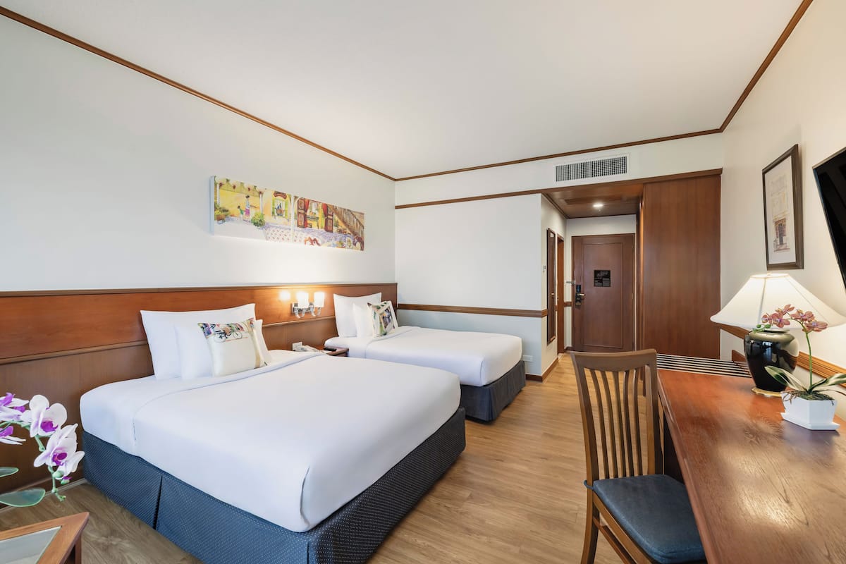 A hotel room with two beds, a wooden dining table, a chair, a TV, and a painting on the wall.