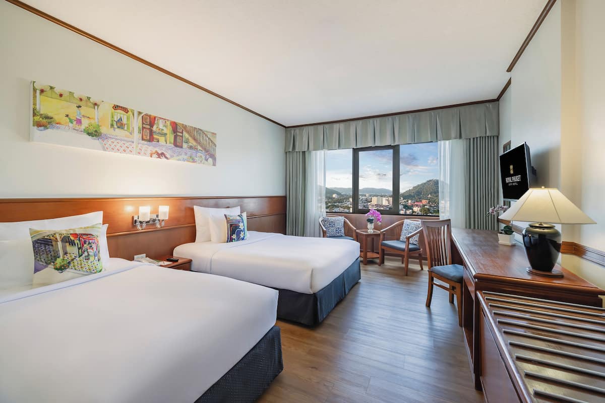 Een hotelkamer met twee bedden, een bureau, een stoel, een televisie en een groot raam met uitzicht op de stad.