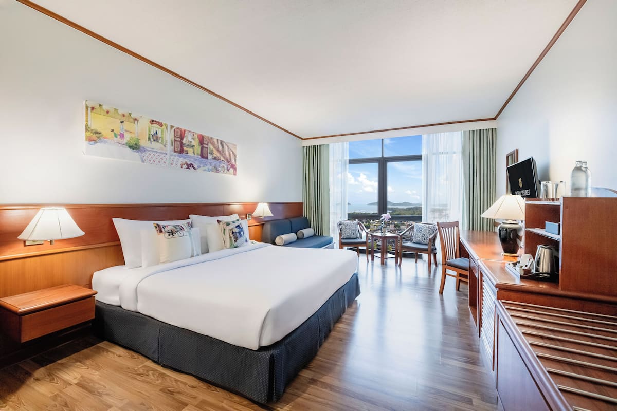 Hotelkamer met een groot bed, een bureau met stoel, een kleine tafel met stoelen en een groot raam met uitzicht.