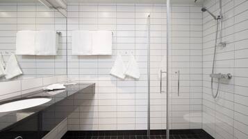 A modern bathroom with a black sink, white tiles, a glass shower enclosure, and white towels.