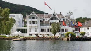 A waterfront hotel with multiple balconies, a dock, and flags. - Thon Hotel Sandven (Kvam)
