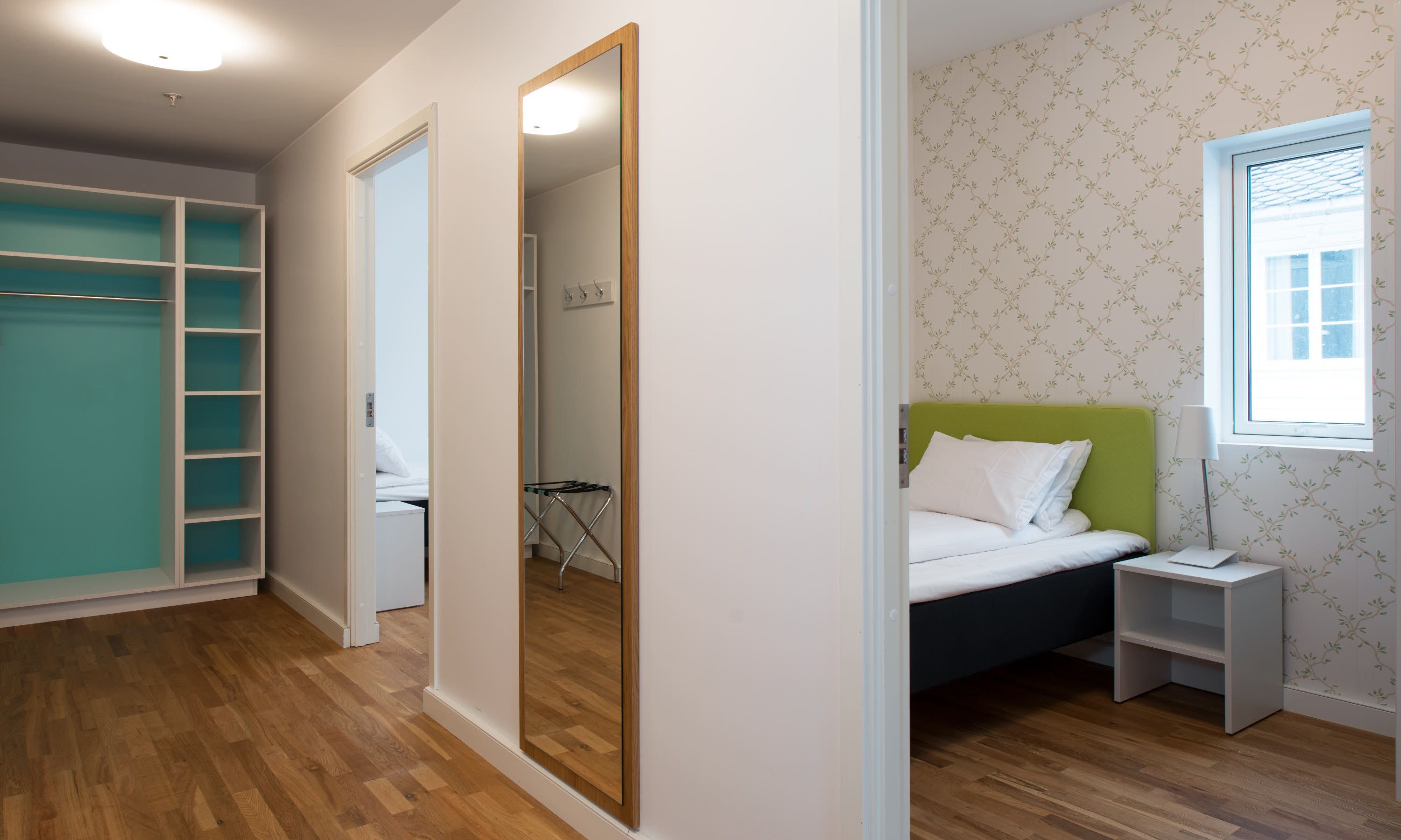 Un dormitorio con cama, mesita de noche, espejo, armario y ventana.