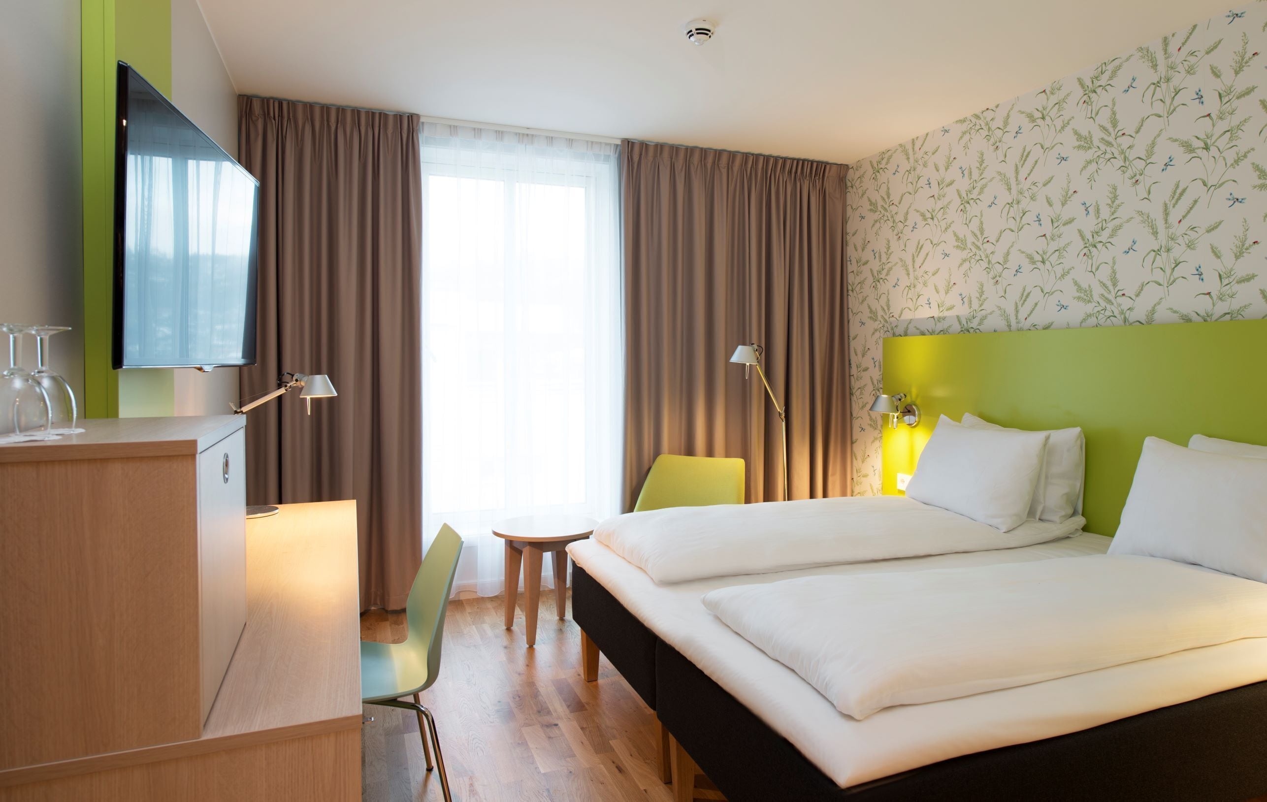 Une chambre d’hôtel équipée d’un lit, d’un bureau, d’une chaise, d’une télévision et d’une fenêtre avec des rideaux.