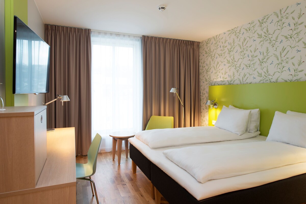 A hotel room with a bed, a desk, a chair, a television, and a window with curtains.
