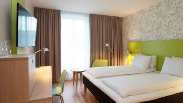 Une chambre d’hôtel équipée d’un lit, d’un bureau, d’une chaise, d’une télévision et d’une fenêtre avec des rideaux.