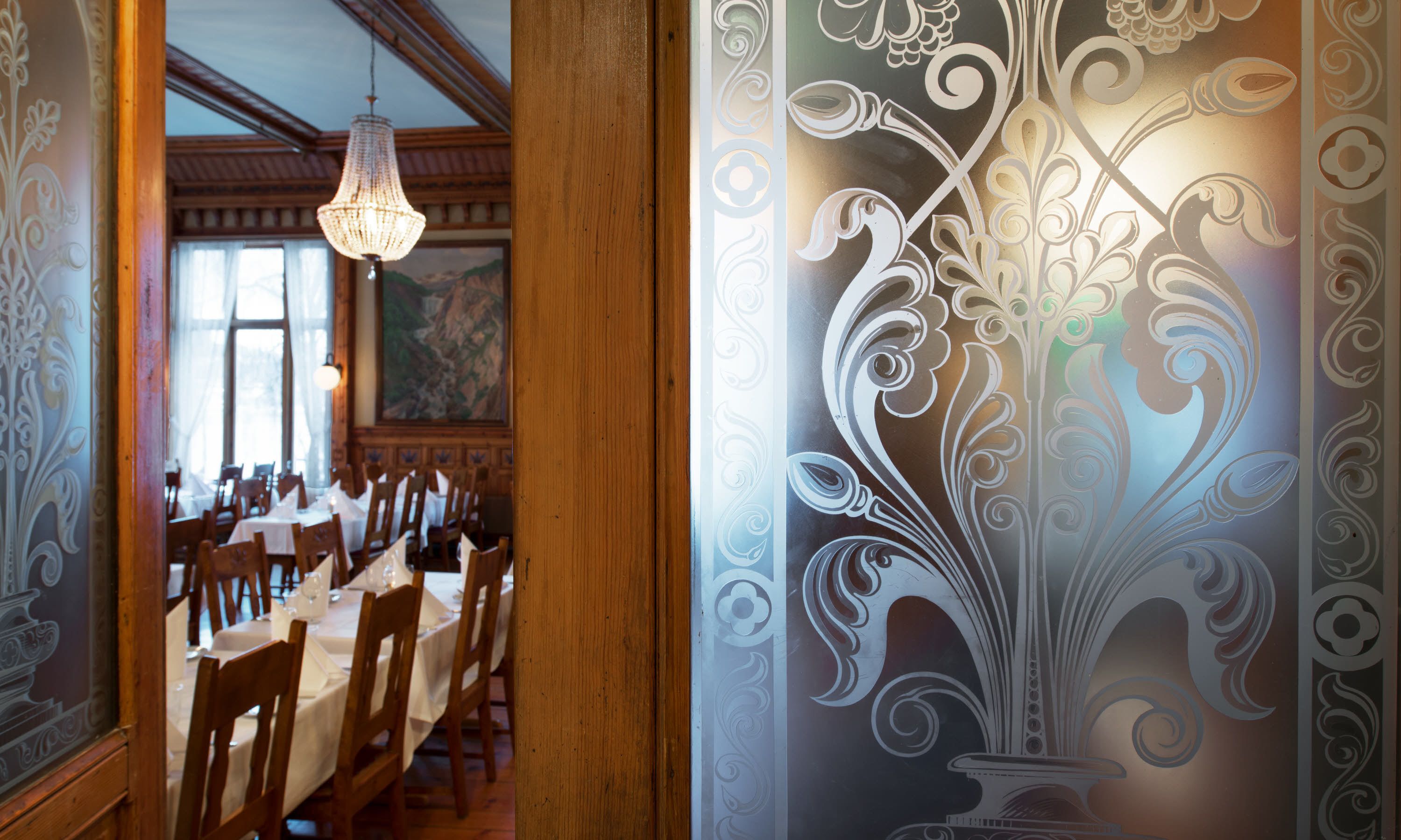 A dining area with wooden tables and chairs, a chandelier, and ornate wall decorations.