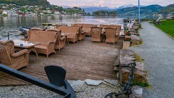 A wooden deck with wicker furniture overlooking a lake, with mountains in the background.