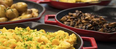 A variety of dishes in red skillets, including scrambled eggs, roasted potatoes, and sautéed mushrooms.