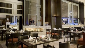 A spacious dining area with multiple tables and chairs, a central counter with a chef, and a modern architectural design with large columns and a high ceiling. - Hotel Santika Premiere Slipi Jakarta (Jakarta)