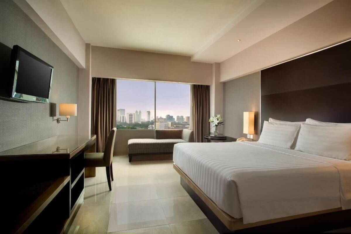 A hotel room with a large bed, a desk, a chair, a TV, and a view of the city skyline.