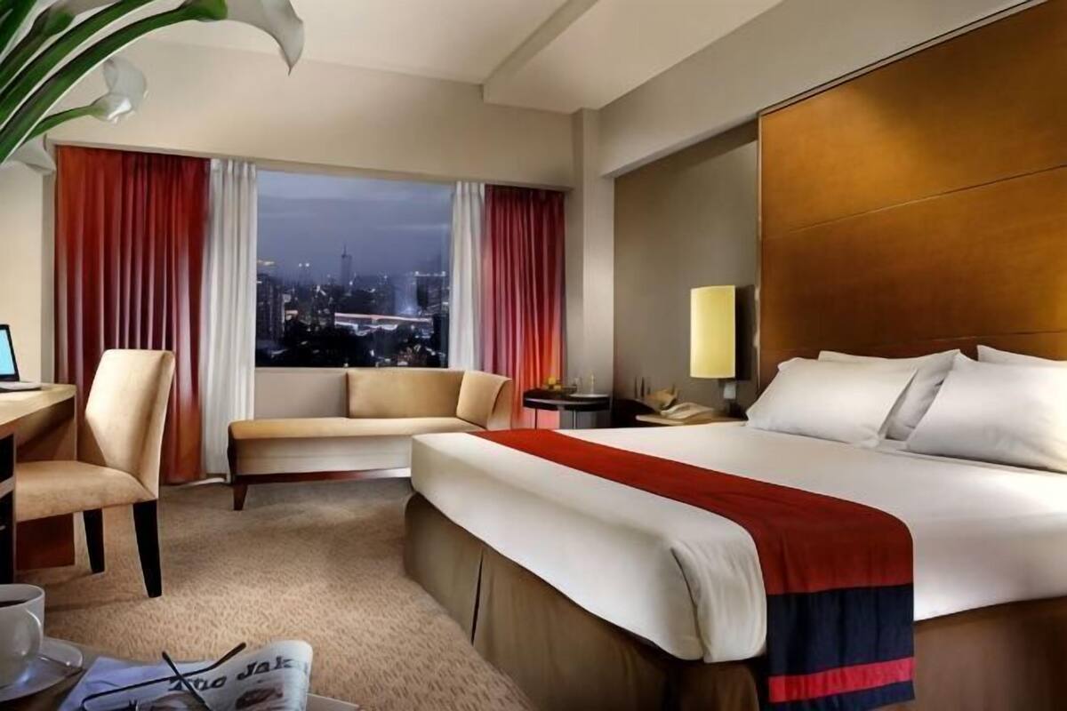 A hotel room with a bed, a desk, a chair, a window with curtains, and a city view.