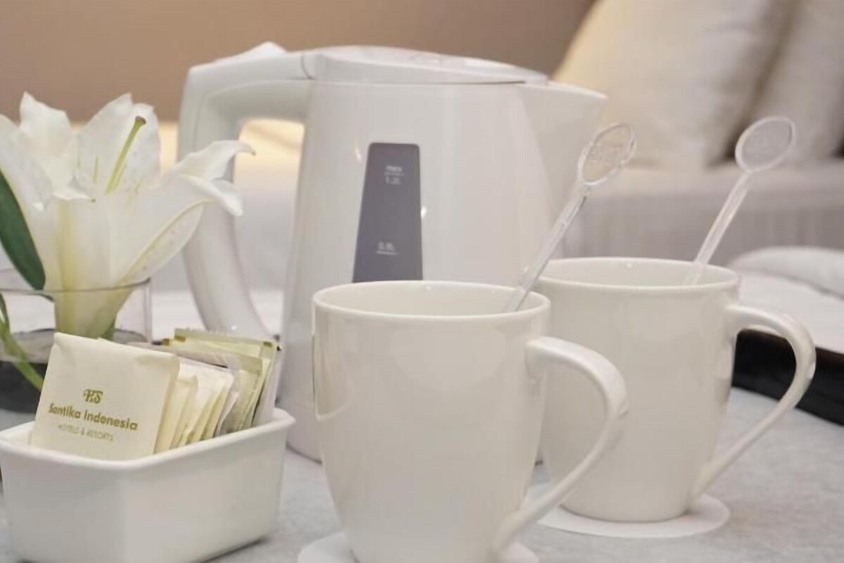 A white coffee maker, two white mugs, a white tray with a card, and a white flower arrangement.