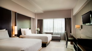 A hotel room with two beds, a desk, a TV, and a large window with curtains. - Hotel Santika Premiere Slipi Jakarta (Jakarta)