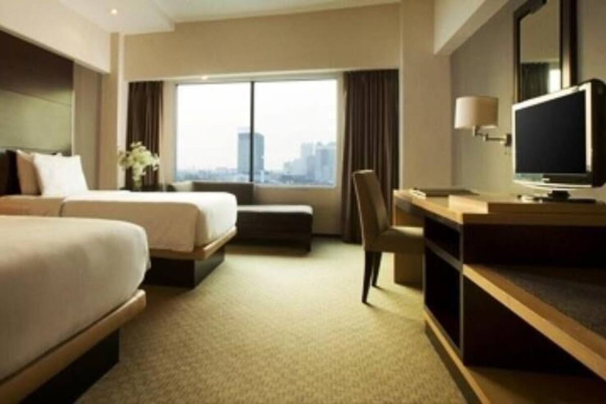 A hotel room with two beds, a desk, a chair, a television, and a large window with a city view.