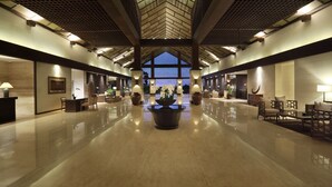 A spacious lobby with a high ceiling, a central floral arrangement, and seating areas on either side. - Grand Luley Manado (Manado)