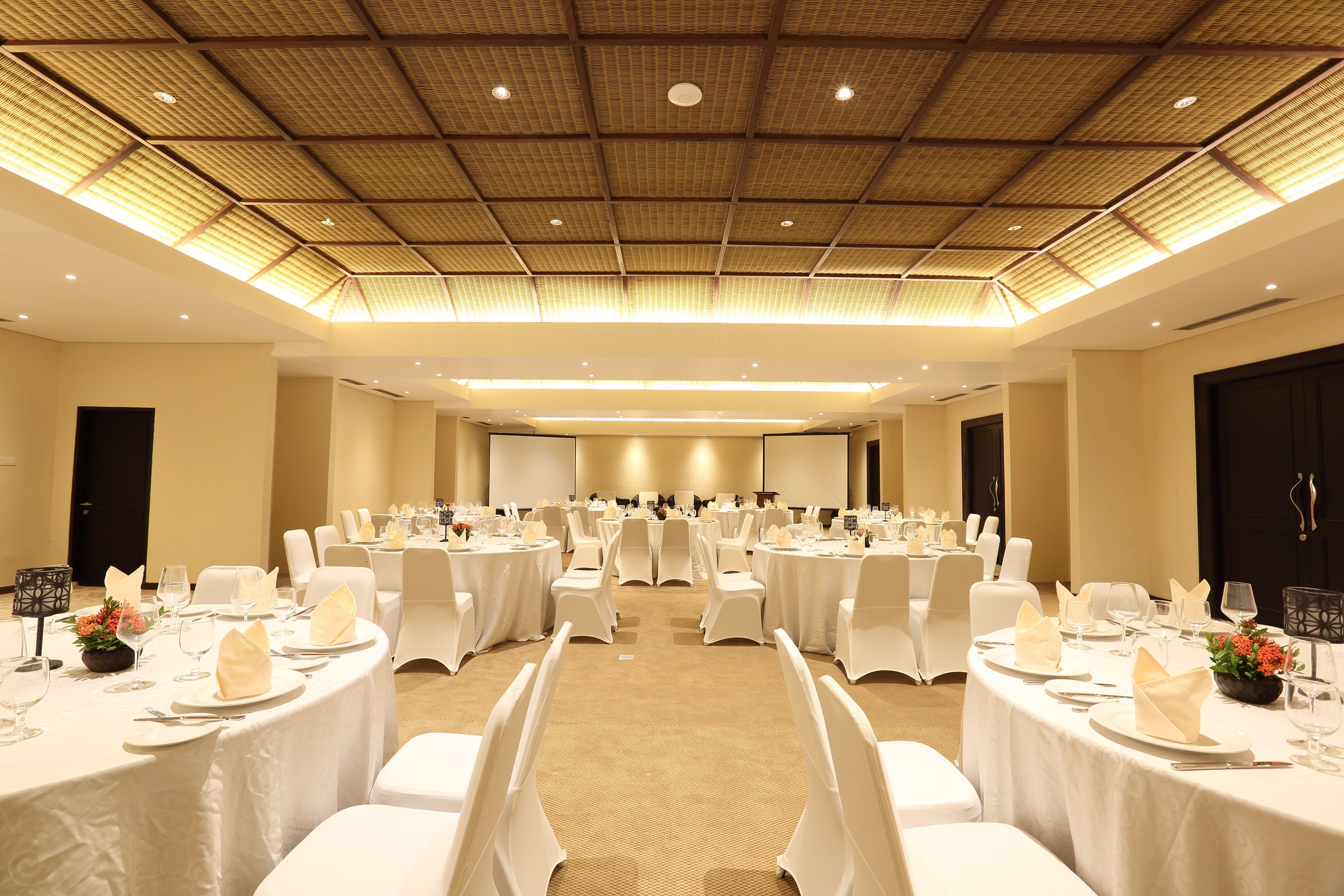 Un salón de banquetes con mesas redondas dispuestas para comer, sillas blancas y un alto techo con un diseño de cuadrícula.