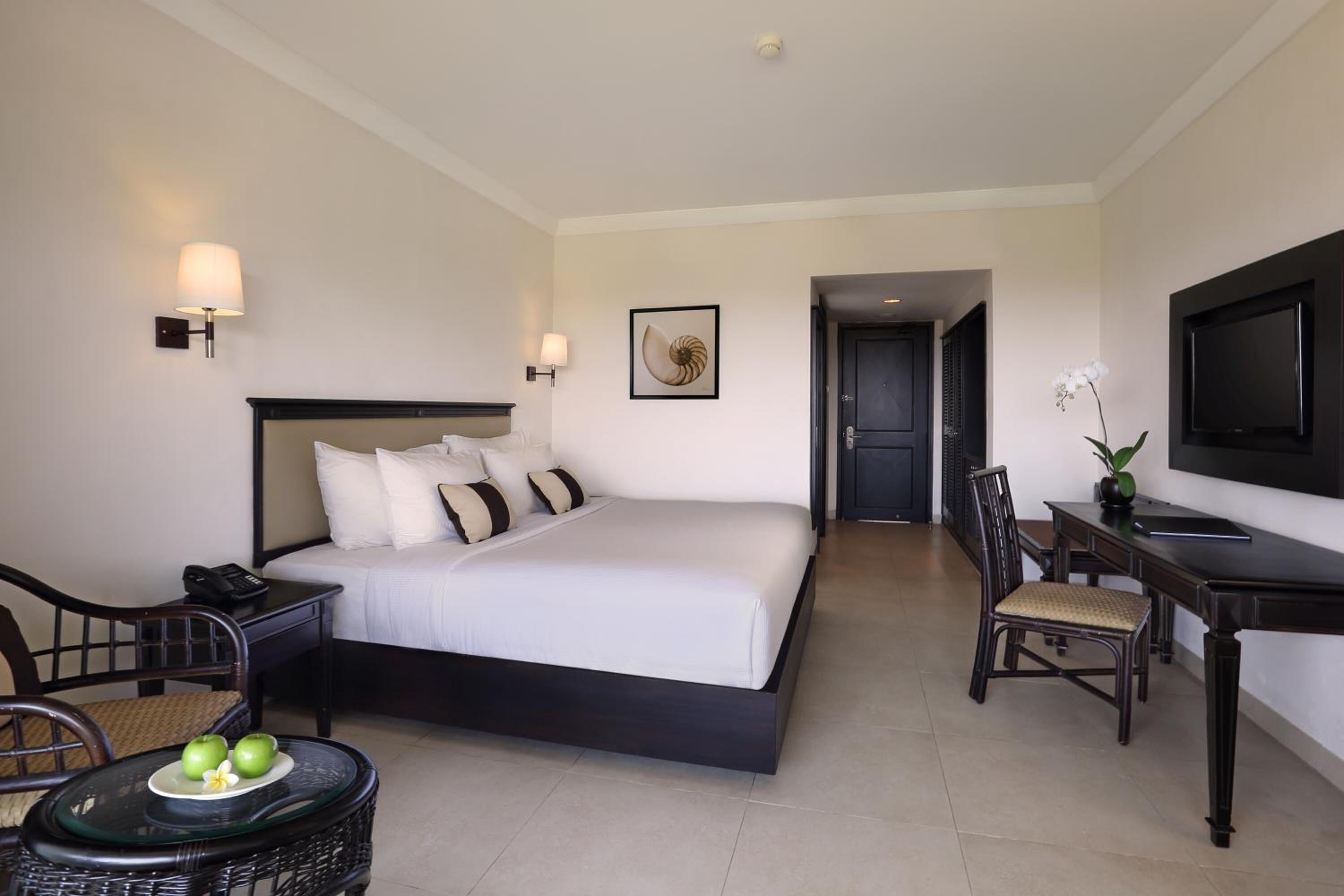 A hotel room with a large bed, bedside tables, a desk with a chair, a television, and a framed artwork on the wall.