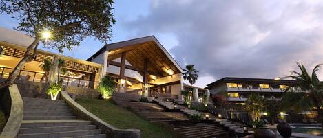 A hotel with a modern architectural design, featuring a prominent staircase leading to the entrance, a pool area, and lush landscaping.