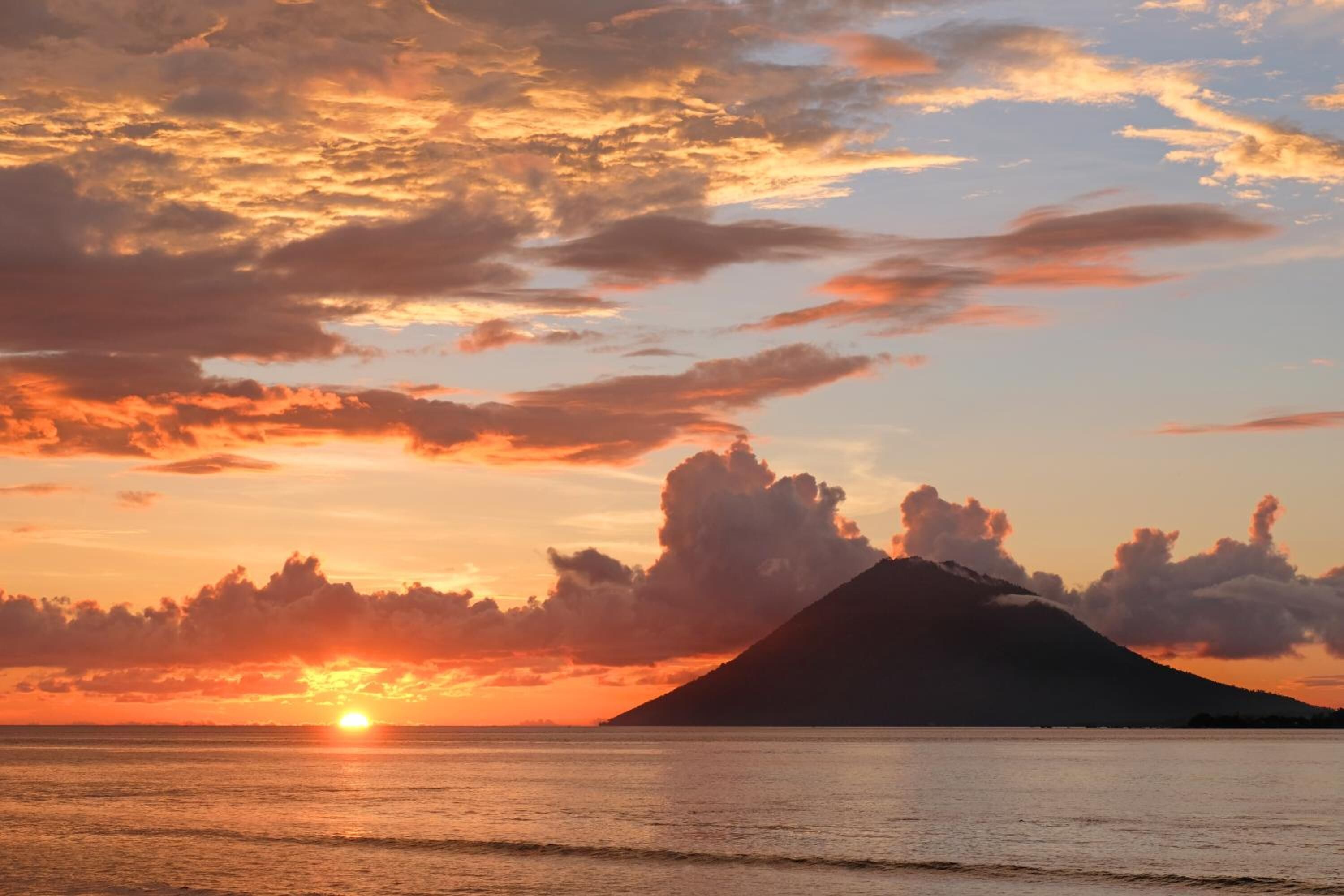 Atardecer sobre un mar tranquilo con el perfil de una montaña.