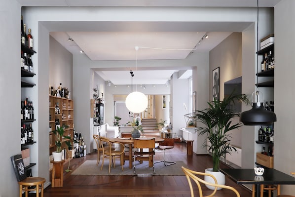 A spacious living area with a dining table, chairs, and a large potted plant. There are shelves with bottles and a staircase leading to another level. - Savoy Hotel (Copenhagen)