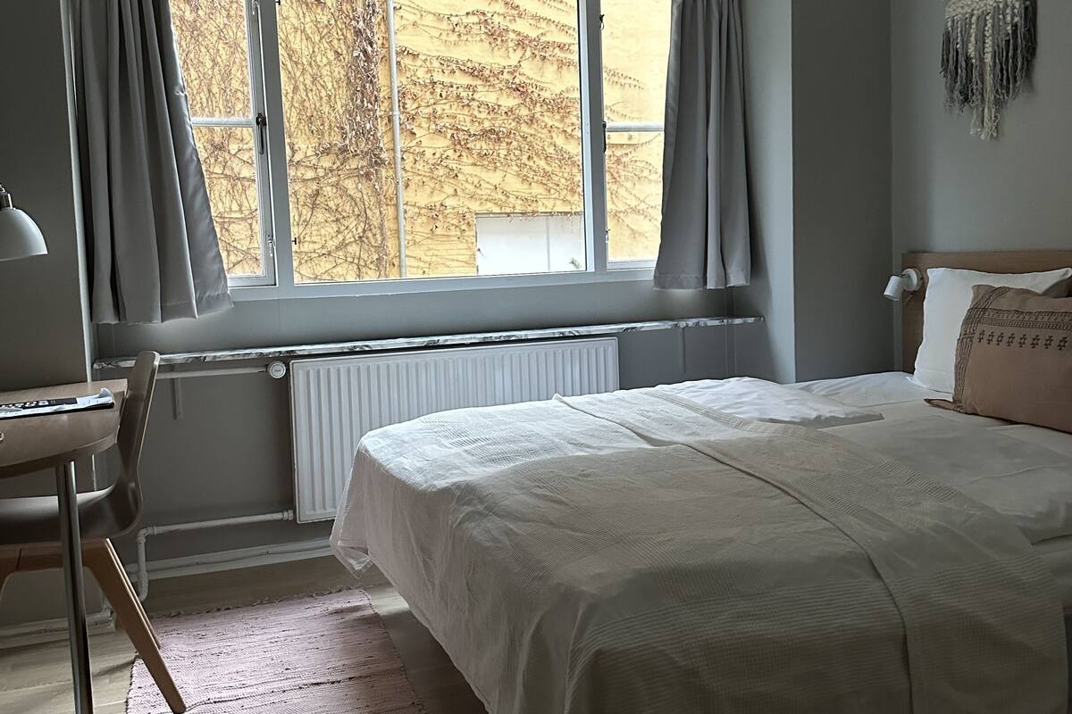 A bedroom with a large bed, a desk, and a window with curtains.