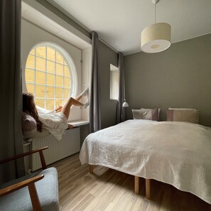 A bedroom with a large bed, a window with curtains, a wooden floor, and a hanging light fixture. - Savoy Hotel (Copenhagen)