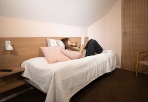 Una cama individual con cabecera de madera, una mesita de noche con lámpara y una silla en una habitación de hotel.